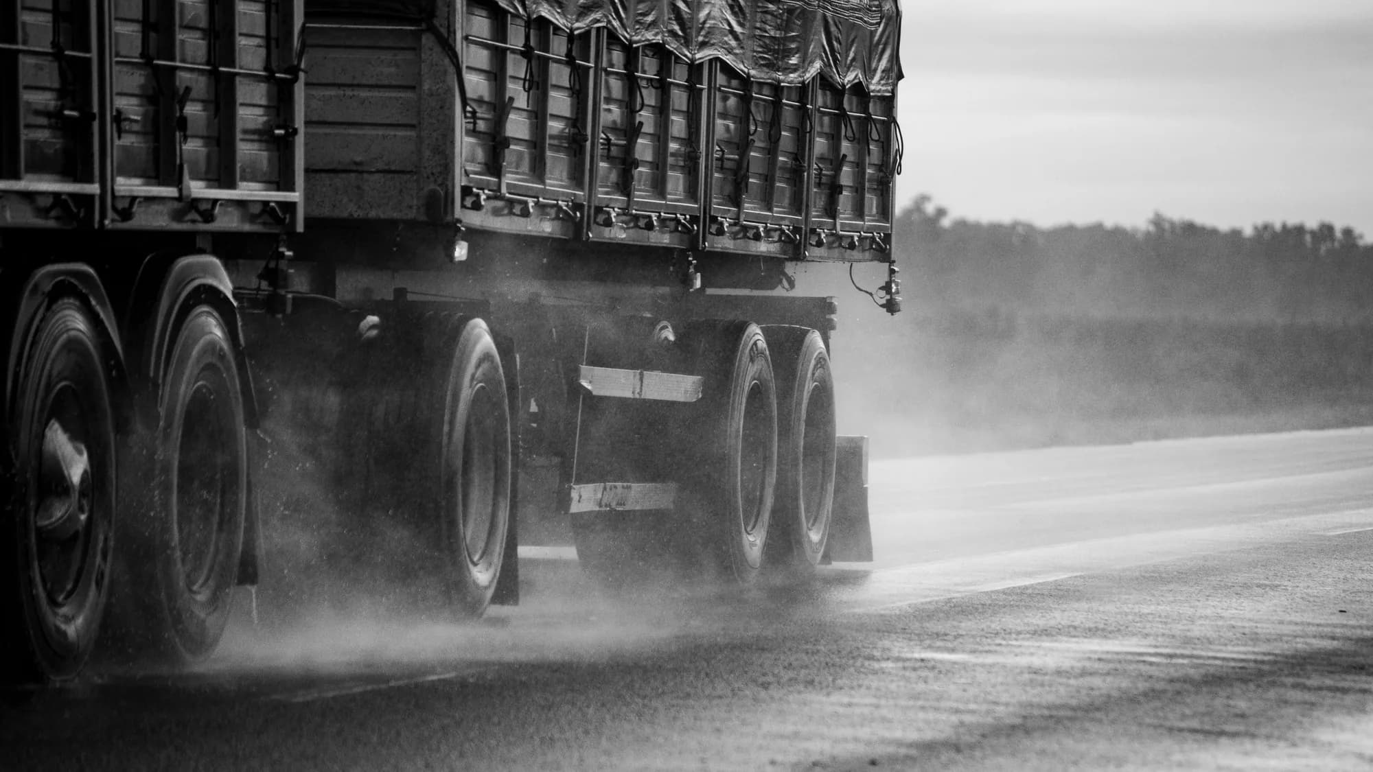 The wheels of a tractor-trailer throwing spray on a wet highway