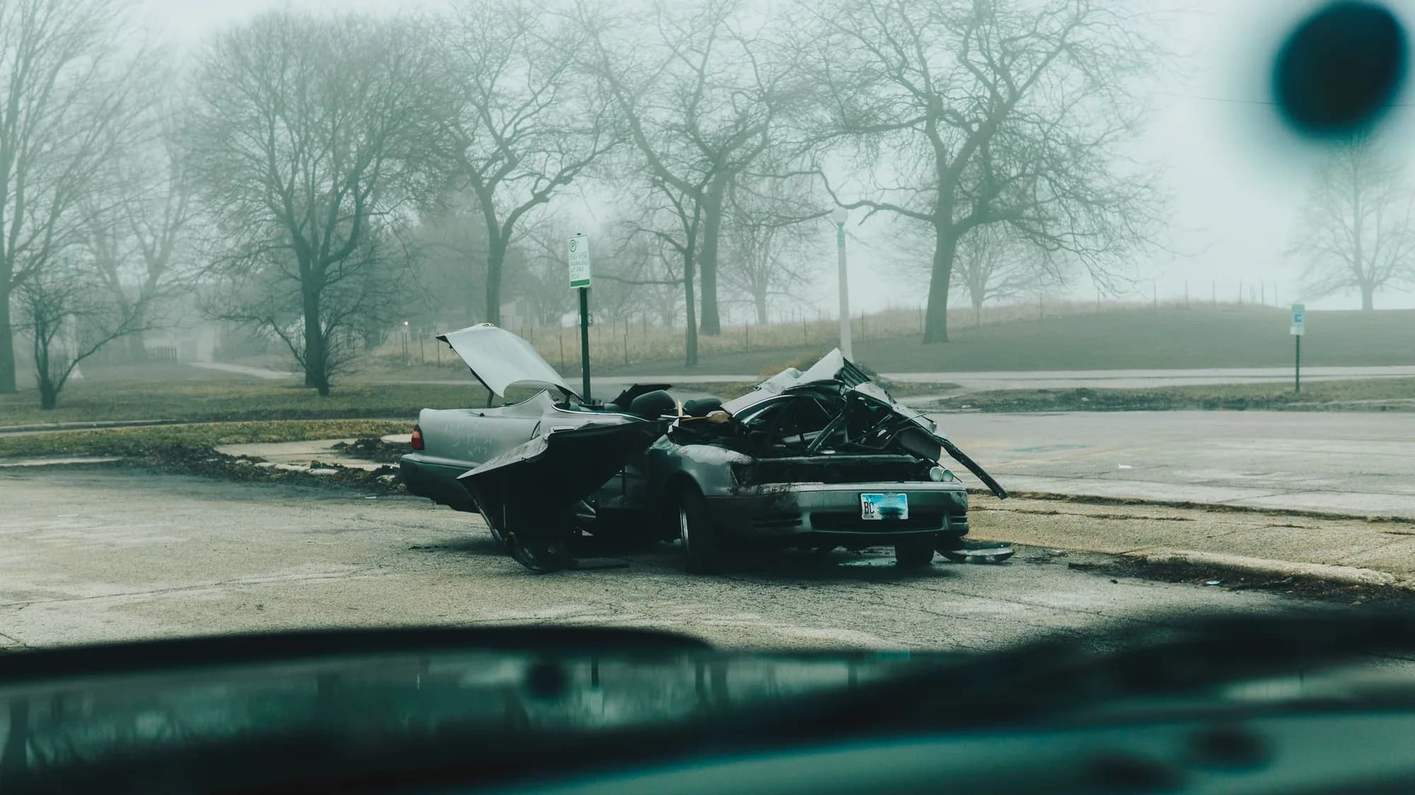 A wrecked car at the roadside in morning fog